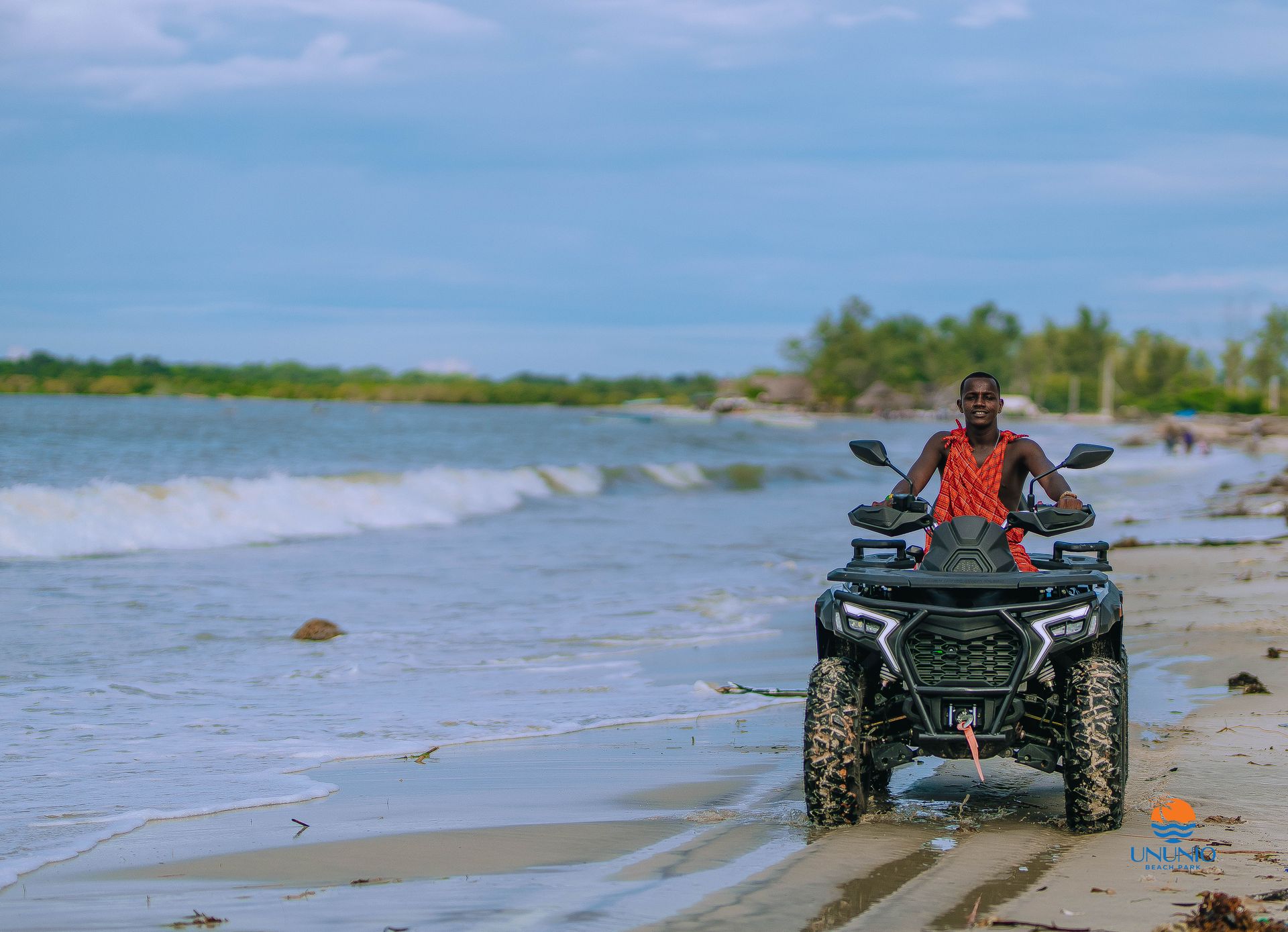 A rider in a red Maasai shuka riding a quad bike along the surf line at Ununio Beach