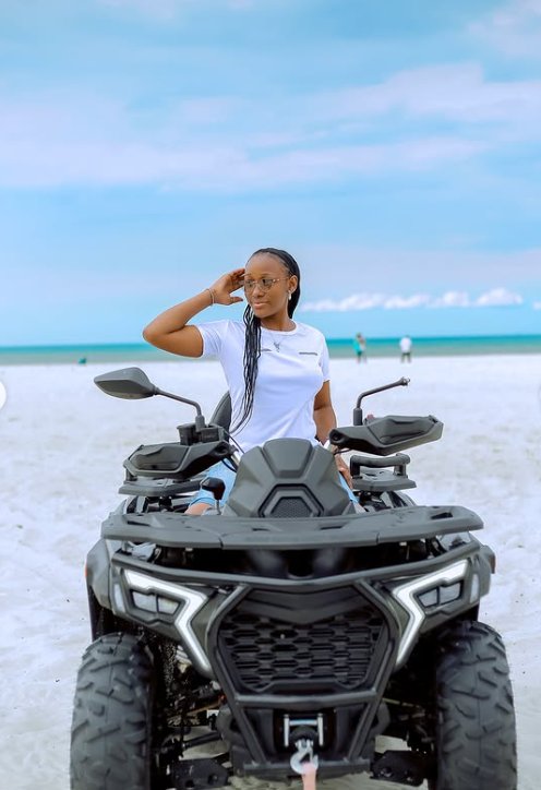 Rider seated on a quad bike on white sand with the turquoise ocean behind